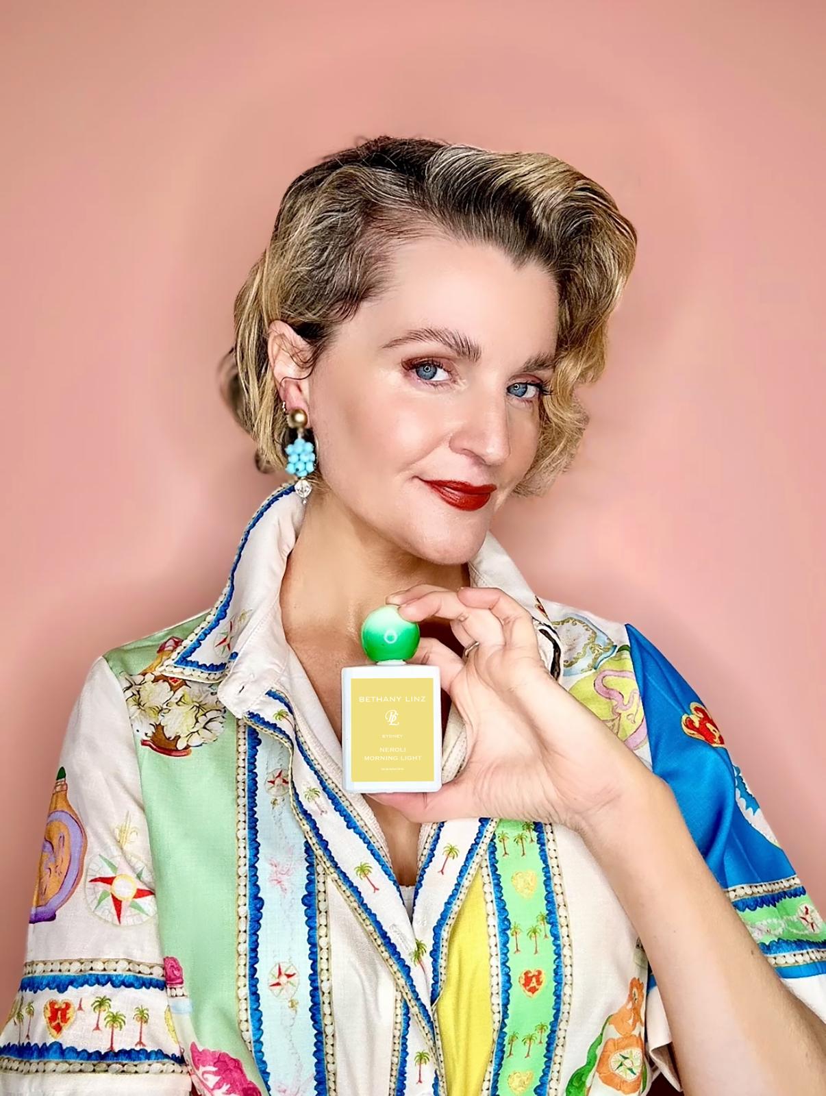 Bethany Linz holding a perfume bottle against a pink background